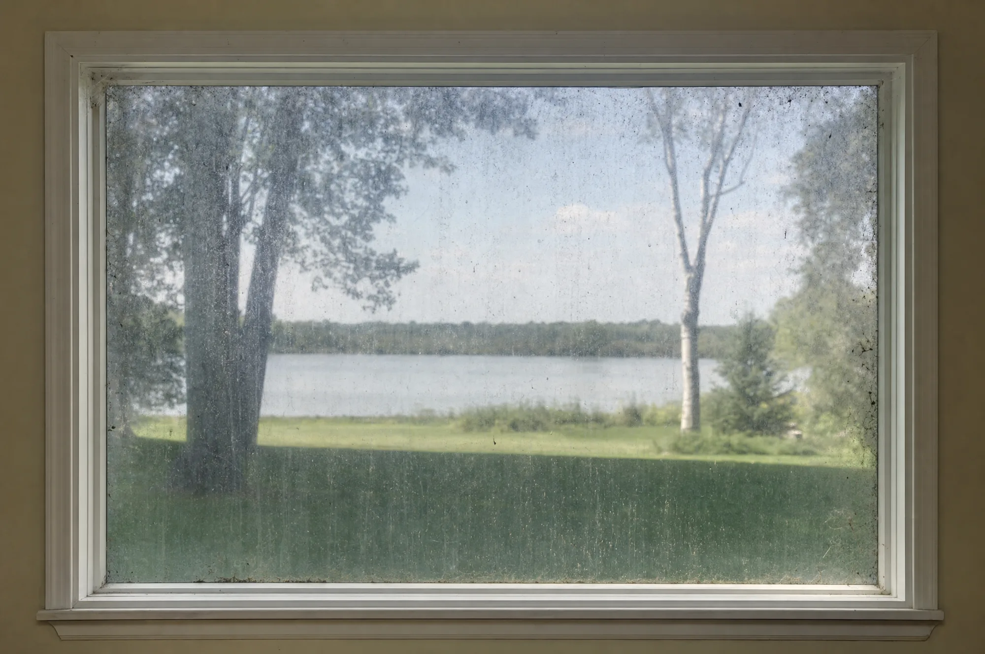 The same window before cleaning, seen from inside, the glass dulled by hard water streaks and dirt